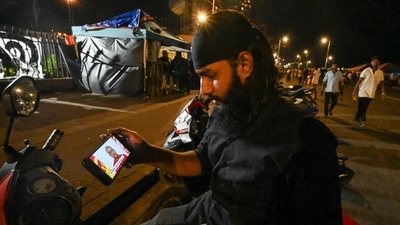 A protester holds a mobile phone while watching an address to the nation by Sri Lanka's President Gotabaya Rajapaksa near the president's office in Colombo. (AFP) A protester holds a mobile phone while watching an address to the nation by Sri Lanka's President Gotabaya Rajapaksa near the president's office in Colombo. (AFP)