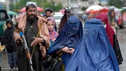 Women walk through the old market as a Taliban fighter stands guard, in the city of Kabul, Afghanistan,