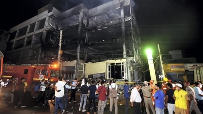 People stand near the charred office building where a massive fire broke out, near the Mundka Metro Station, in West Delhi. (PTI) People stand near the charred office building where a massive fire broke out, near the Mundka Metro Station, in West Delhi. (PTI)