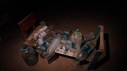 Empty plastic bottles and cups are placed on a wooden bench in the makeshift shelter of a kindergarten's basement, where she has been living with other six people for more than two months.