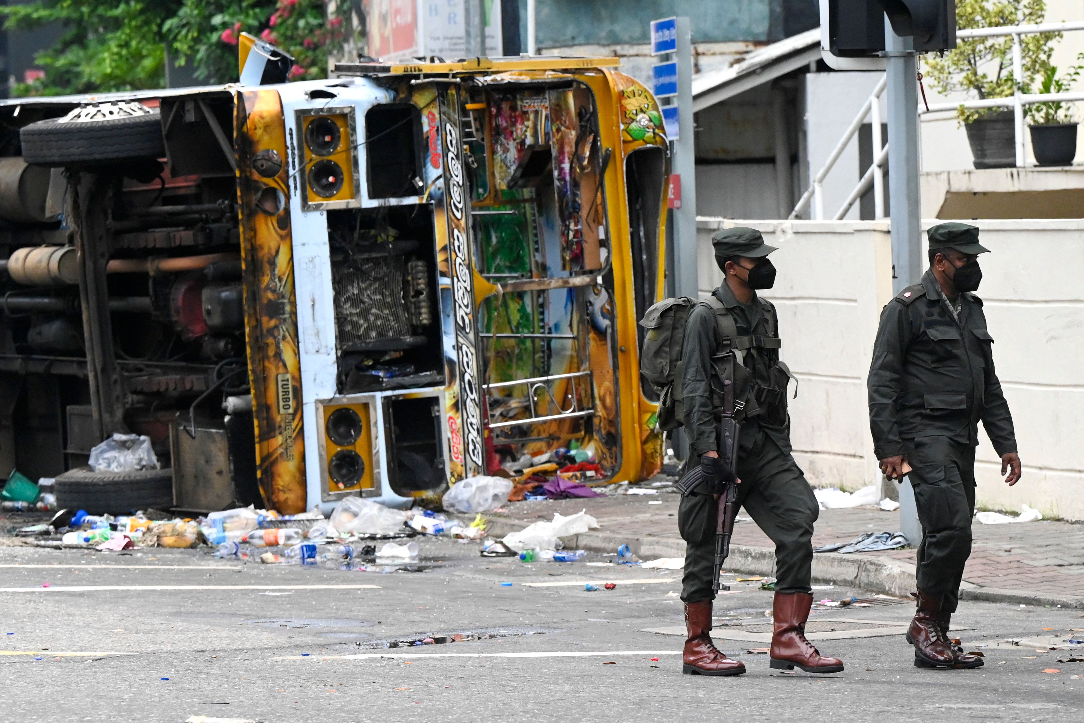 Sri Lankan soldiers walk past a burnt bus near Sri Lanka's former prime minister Mahinda Rajapaksa's official residence, a day after it was torched by protesters in Colombo on May 10, 2022. (AFP)