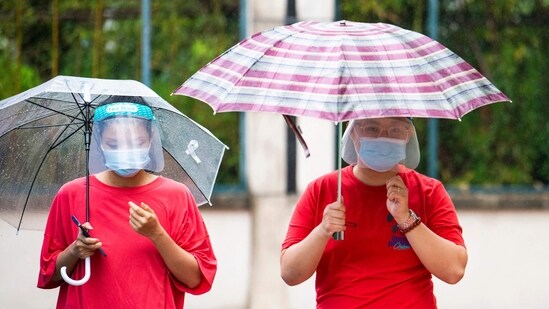 Local residents queue with umbrellas for nucleic acid tests for the Covid-19 coronavirus in a compound under lockdown in the Pudong district in Shanghai.(Photo by LIU JIN / AFP)
