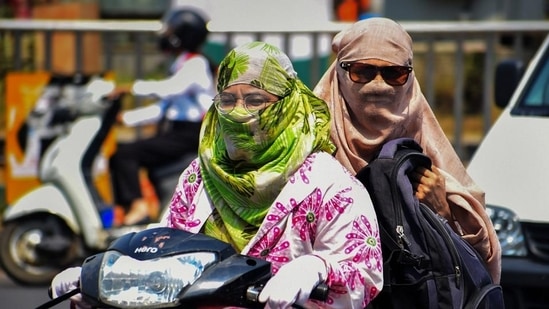 Commuters use scarves to shield themselves from the heat while riding a two-wheeler in Prayagraj. (PTI)