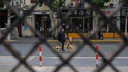Um homem anda de bicicleta em uma rua vista através de uma cerca de um complexo fechado durante um bloqueio de coronavírus Covid-19 no distrito de Jing'an, em Xangai.  (AFP)