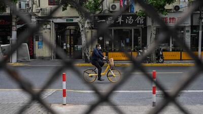 A man rides a bicycle on a street seen through a fence of a compound in lockdown during a Covid-19 coronavirus lockdown in the Jing'an district, in Shanghai. (AFP)