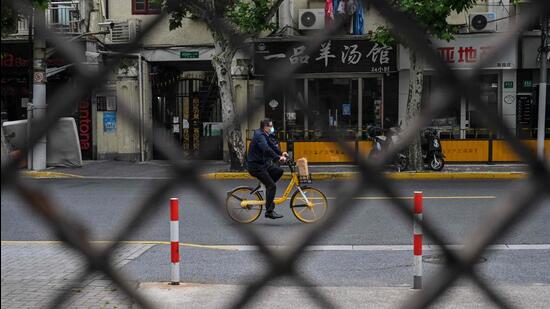 A man rides a bicycle on a street seen through a fence of a compound in lockdown during a Covid-19 coronavirus lockdown in the Jing'an district, in Shanghai. (AFP)