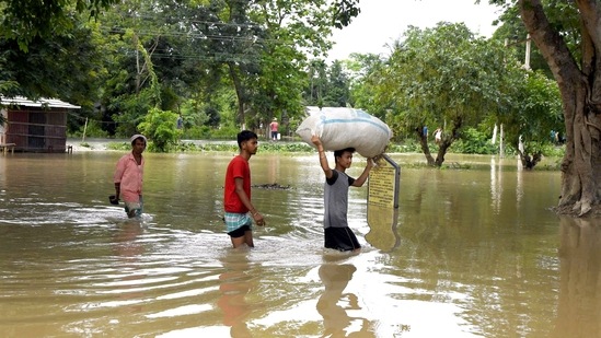 Villagers wade through the waterlogged area following heavy rainfall in Assam's Darrang district. (ANI Photo)