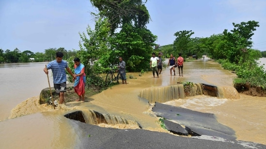  People wade through a road damaged by flood waters after heavy rains in Nagaon district, Assam.(AFP)