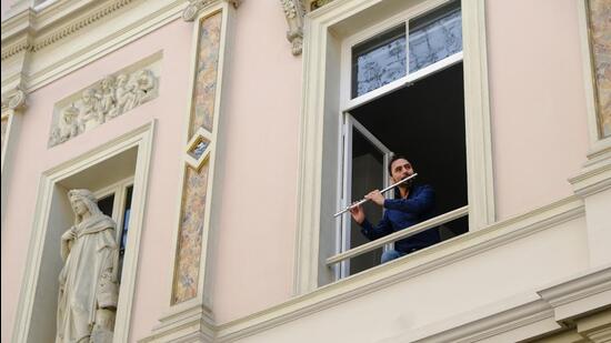 A flautist performs at his window for his neighbours in Brussels, Belgium, during the lockdown in 2020. This sort of communal form of art making like the “balcony and courtyard concerts” in his story, The Mask, appeals to Carlo Pizzati. (Shutterstock)