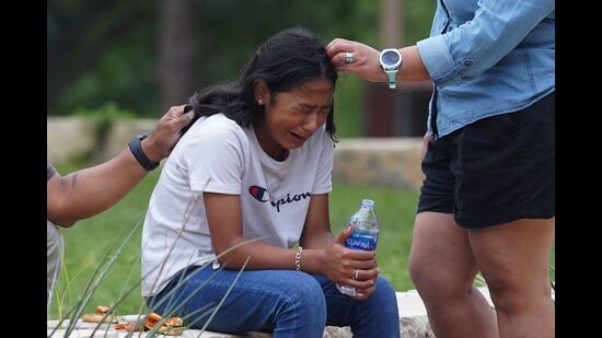 A girl cries, comforted by two adults, outside the Willie de Leon Civic Center where grief counseling will be offered in Uvalde, Texas, May 24, 2022 (AFP)