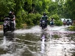 Commuters drive past a fallen tree branch on a waterlogged street after a storm in New Delhi on May 30, 2022.