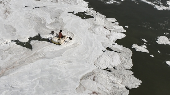 A man rides a makeshift boat through toxic foam floating in Yamuna river, on World Environment Day, at ITO, in New Delhi, Sunday.(PTI)