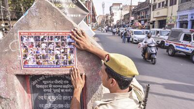 A police personnel sticks a poster of the accused involved in a clash in Kanpur, on Monday. (PTI) A police personnel sticks a poster of the accused involved in a clash in Kanpur, on Monday. (PTI)