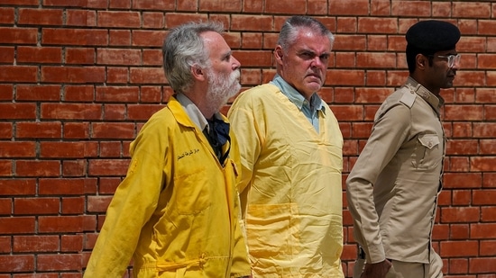 Jim Fitton of Britain, left, and Volker Waldmann of Germany, center, wearing yellow detainees’ uniforms and handcuffed are escorted by Iraqi security forces, outside a courtroom, in Baghdad, Iraq, Sunday.(AP)