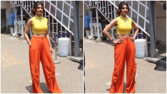 Shilpa chose a yellow sleeveless fitted top featuring a round neckline, minimal floral pattern on the front and cropped hem length flaunting the star's toned midriff. She wore the short blouse with high-waisted pants in an orange hue, floor-grazing hem, cinched details on side patch pockets and a flared silhouette.(HT Photo/Varinder Chawla)
