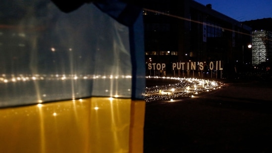 A demonstrator holds an Ukrainian flag in front of a sign reading "Stop Putin's oil" during a vigil for Ukraine near the European Union (EU) headquarters in Brussels.(AFP)