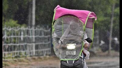 A two-wheeler rider finds a unique way to avoid being drenched, as rain Gods smile upon Ludhiana on Friday. (Gurpreet Singh/HT)