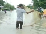 A man laying a fishing net in waterlogged street in Assam's Kamrup district.(ANI)