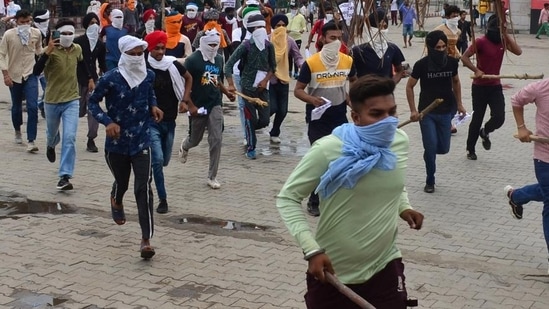 Armed with sticks and faces covered, youths rushing towards to the entrance of Ludhiana railway station, where they later burnt a block hut and vandalised furniture, on Saturday during a protest against Agnipath scheme. (Gurpreet Singh/HT)