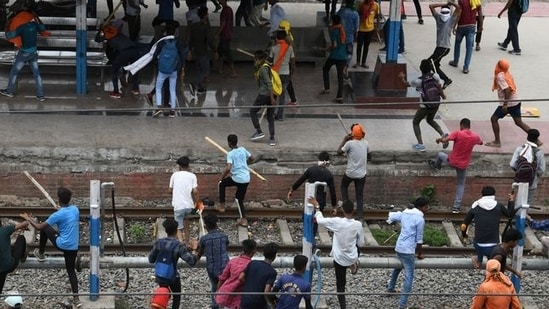 Protestors carrying sticks run at a railway station during a protest against the Agnipath scheme in Patna, Bihar.(Reuters)