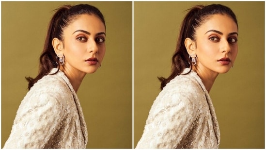Rakul Preet paired a white long top with a plunging neckline and a white belt detail around the waist. She added a white pair of trousers to her look that came detailed in silver embellishments. In white ear studs from Solasta Jewellery, Rakul Preet accessorised her look.(Instagram/@rakulpreet)