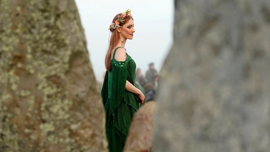 A woman dressed in pagan attire watches the sun rise during the Summer Solstice festivities at Stonehenge in Wiltshire, England on June 21, 2022. Plenty others awakened early and made the trip there just to soak up the atmosphere.(AP)