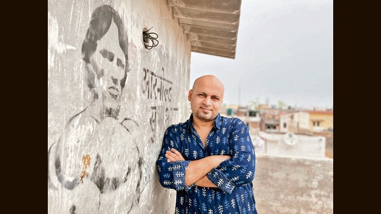 Mohit Suneja stands next to the mural where he wrote Arnold Subhashnagar alongside a sketch of the actor.