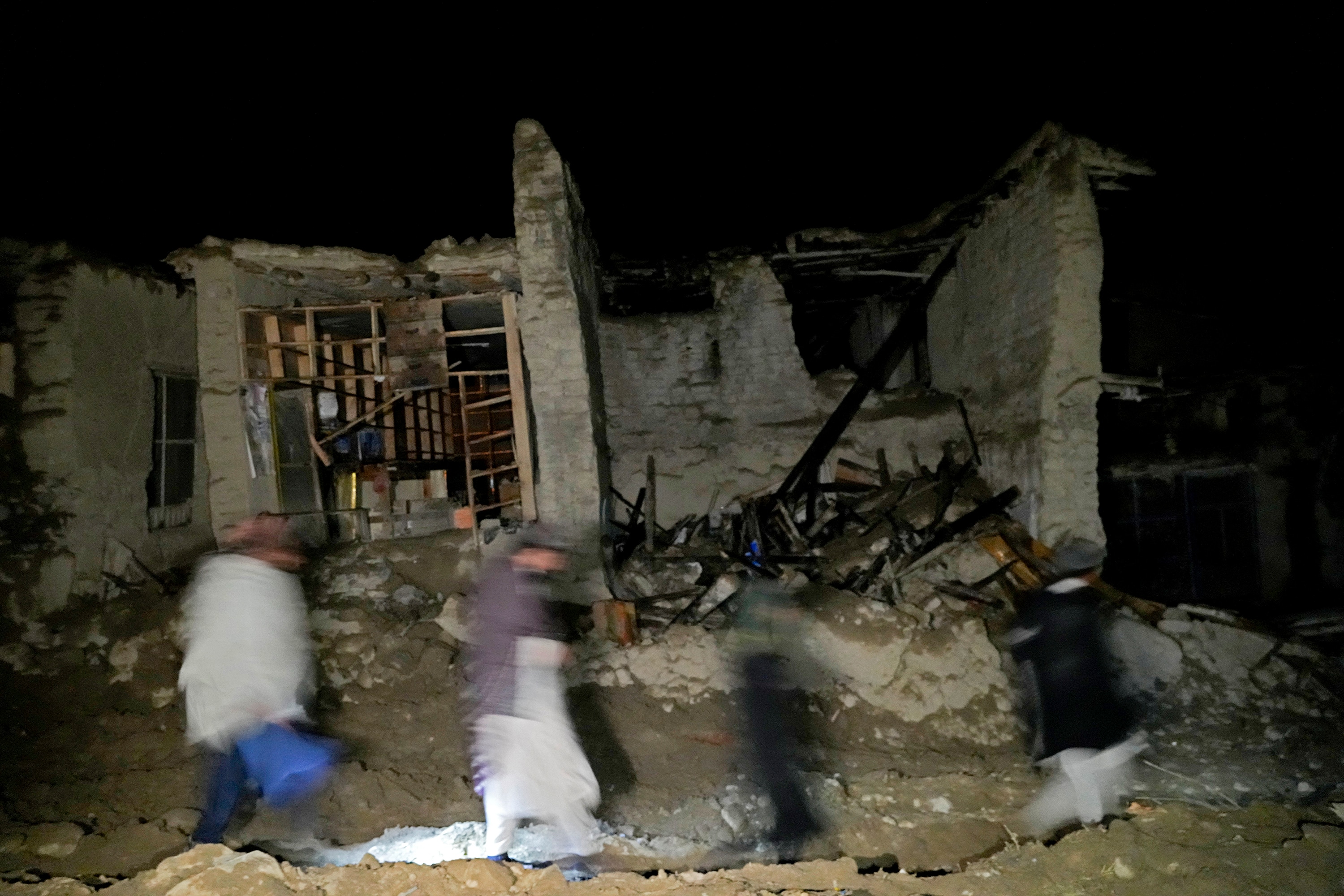 Afghans walk by a destroyed housein the village of Gyan, in Paktika province, on June 22, 2022.&nbsp; (AP)