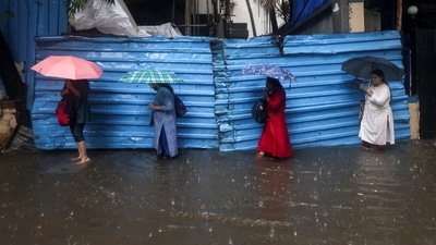 Women attempt to cross a waterlogged street amid heavy rainfall. (REUTERS)