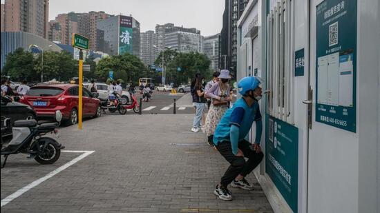 A healthcare worker in protective gear collects a sample from a resident at a Covid-19 testing booth in Beijing, China, on Tuesday. (Bloomberg)