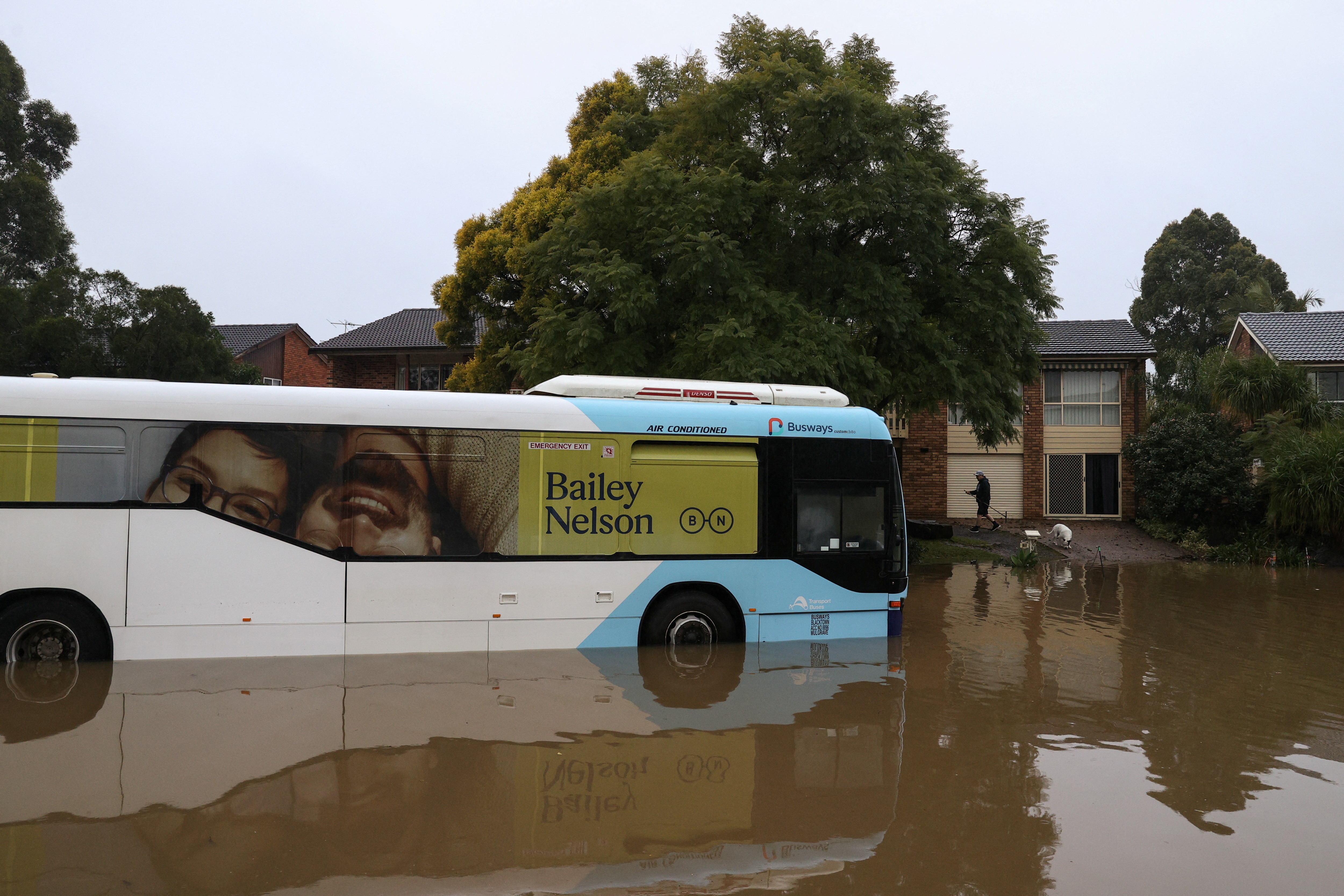 A man clears debris from a driveway near a bus inundated by floodwaters on a residential street, following heavy rains and severe flooding in the McGraths Hill suburb of Sydney, on July 6, 2022.&nbsp; (Reuters photo)