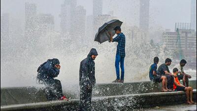 People sit by the seashore during monsoon rains at Marine Drive in Mumbai. (PTI Photo)