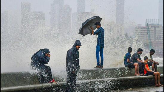 People sit by the seashore during monsoon rains at Marine Drive in Mumbai. (PTI Photo)