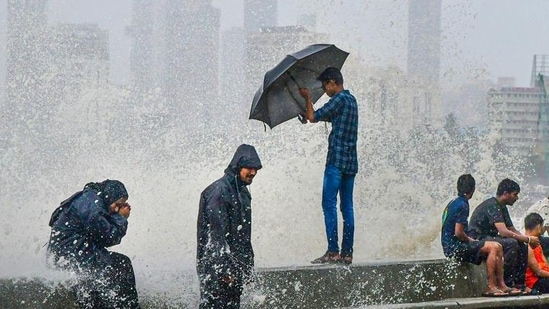 People sit by the seashore during monsoon rains at Marine Drive in Mumbai. (PTI Photo)