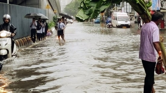 People wade through waterlogged road amid heavy rainfall, at Khodadad Circle, Dadar , in Mumbai on July 6, 2022.&nbsp;