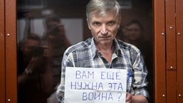 Alexei Gorinov stands with a poster reading ""Do you still need this war?" inside a glass cell during the verdict hearing in his trial at a courthouse in Moscow on July 8, 2022.