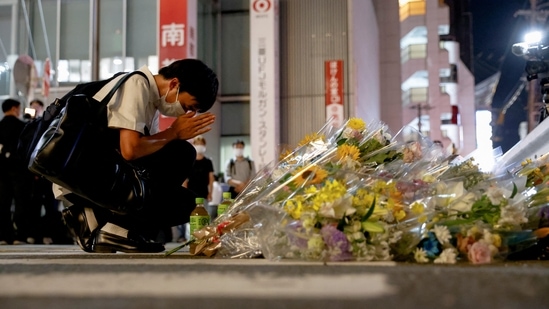 A person prays next to flowers laid at the site where late former Japanese PM Shinzo Abe was shot while campaigning for a parliamentary election, near Yamato-Saidaiji in Nara, western Japan, July 8, 2022. REUTERS/Issei Kato