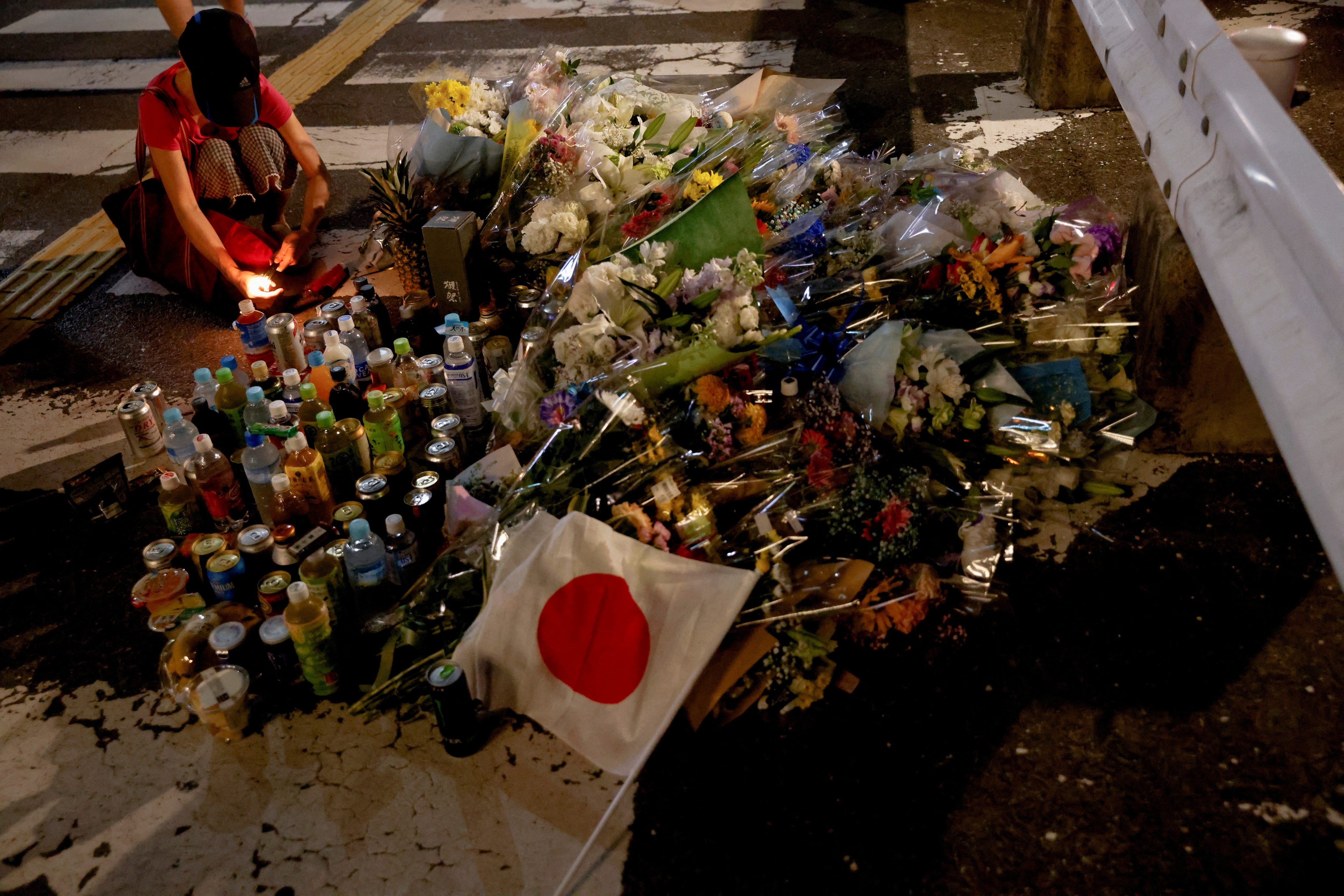 A person pays respects next to tributes laid at the site where Shinzo Abe was shot while campaigning for a parliamentary election, near Yamato-Saidaiji station in Nara.&nbsp; (Reuters)
