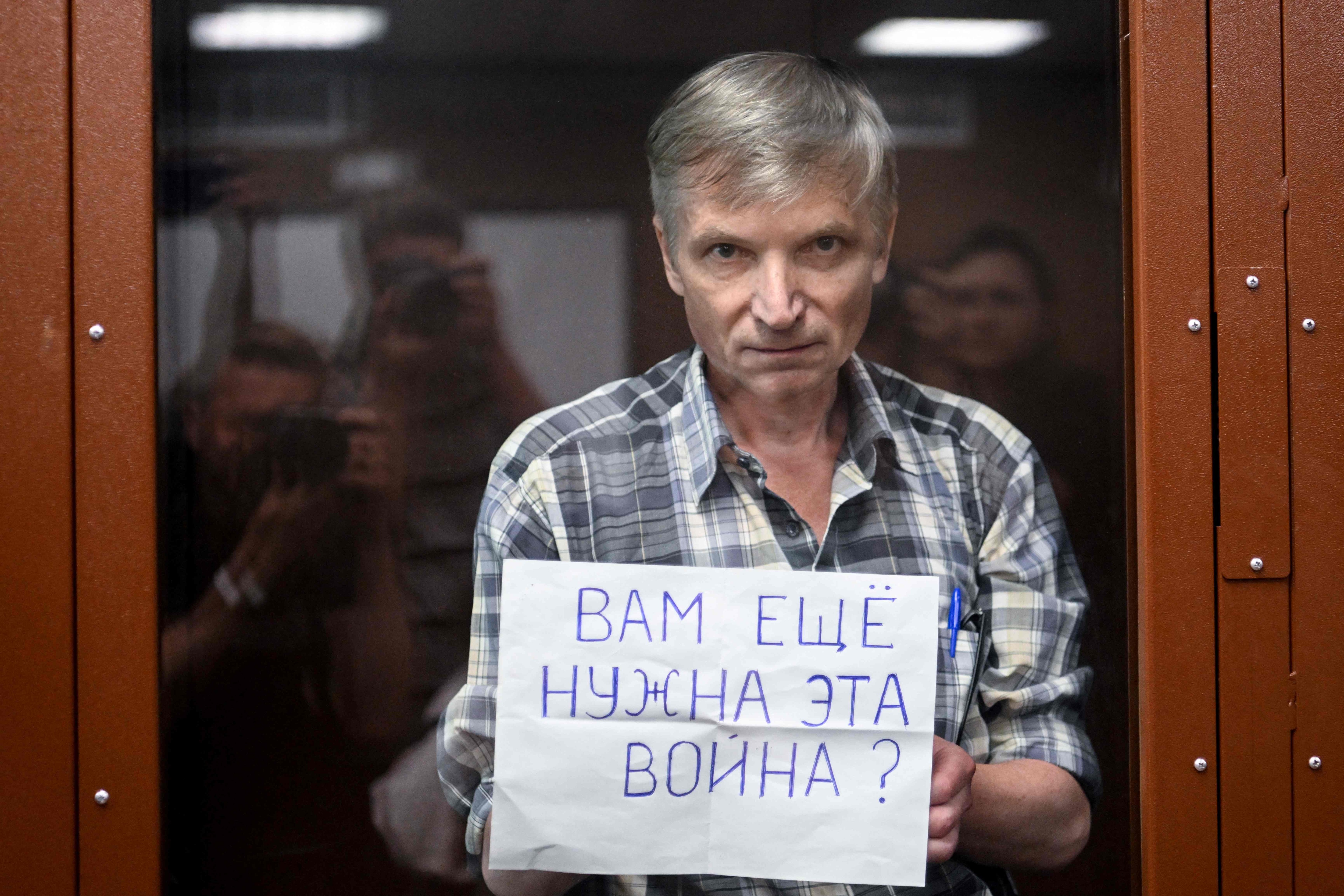Alexei Gorinov stands with a poster reading ""Do you still need this war?" inside a glass cell during the verdict hearing in his trial at a courthouse in Moscow on July 8, 2022. (AFP)