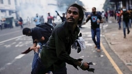 A demonstrator throws back a tear gas grenade towards police members as police use tear gas and water cannons to disperse demonstrators near President's residence during a protest in Colombo, Sri Lanka,