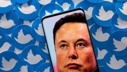 Uma imagem de Elon Musk é vista no smartphone colocada em logotipos impressos do Twitter.