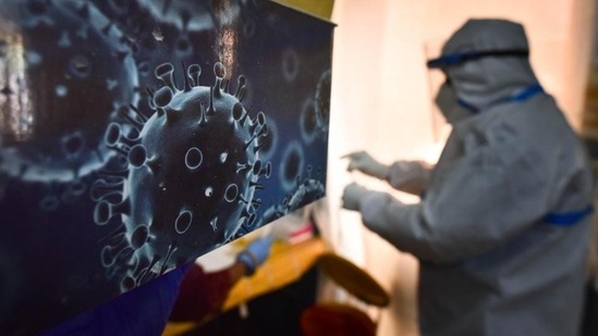 An illustration of the novel coronavirus seen next to a health care worker at a Covid-19 testing centre in New Delhi. (HT PHoto)