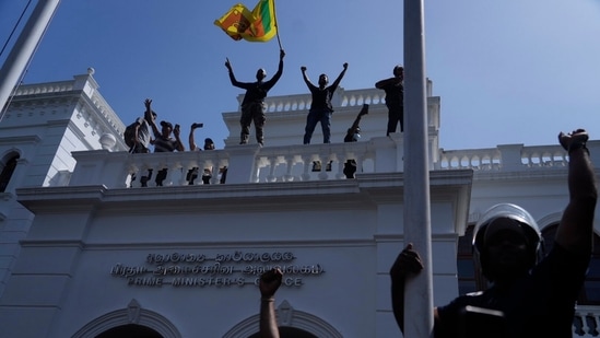 Sri Lankan protesters wave the national flag from the roof of prime minister Ranil Wickremesinghe 's office, demanding he resign after president Gotabaya Rajapaksa fled the country amid economic crisis in Colombo.(AP)