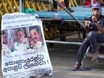 A protester drinks a cup of tea as she sits by a defaced poster carrying portraits of ousted president Gotabaya Rajapaksa, center, and his brothers at the entrance to president's office in Colombo, Sri Lanka on Friday.(AP) A protester drinks a cup of tea as she sits by a defaced poster carrying portraits of ousted president Gotabaya Rajapaksa, center, and his brothers at the entrance to president's office in Colombo, Sri Lanka on Friday.(AP)