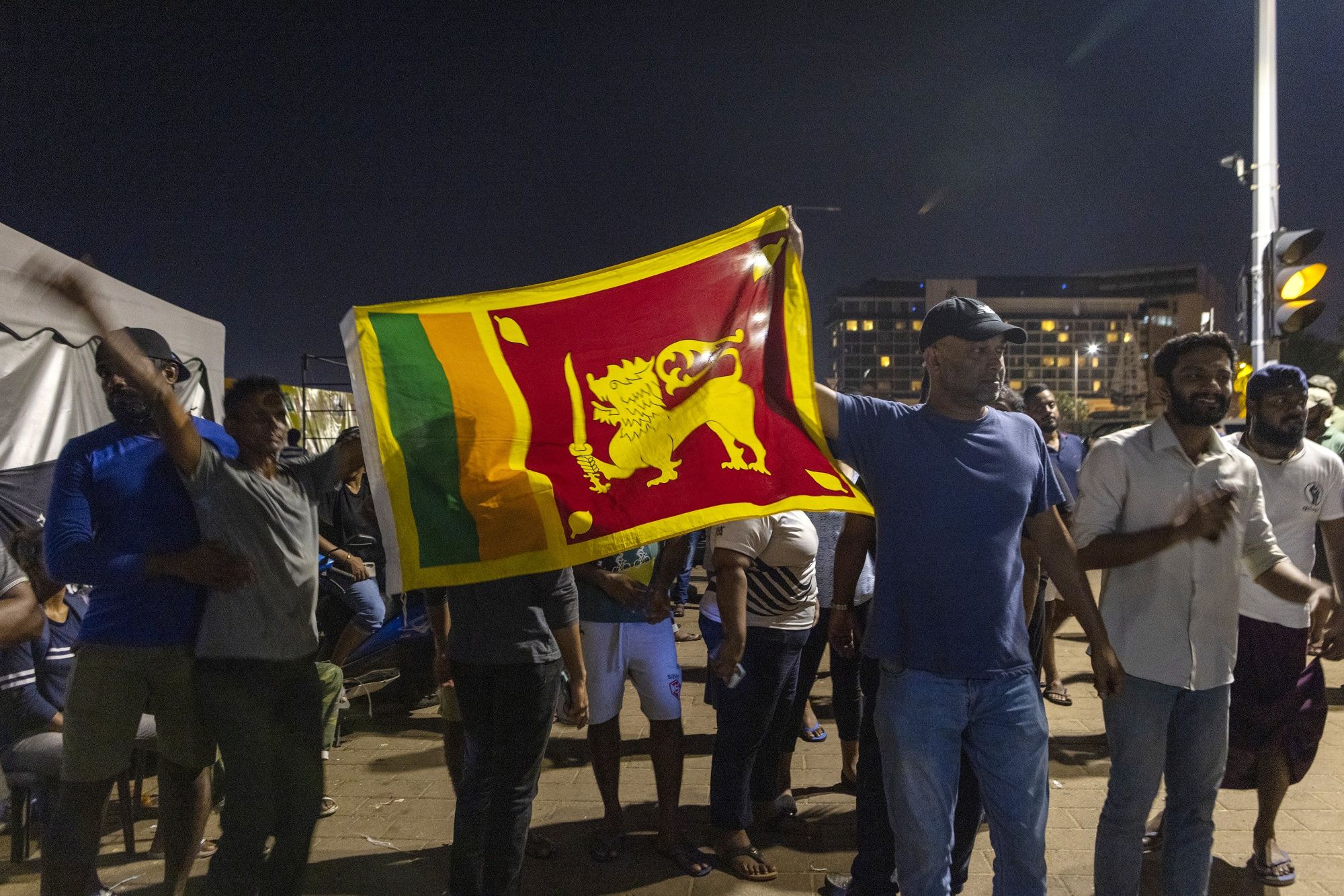 Demonstrators hold up a Sri Lankan flag after hearing news that President Gotabaya Rajapaksa, emailed a letter of resignation, at a protest site close to the president's office in Colombo, on Thursday, (Bloomberg)