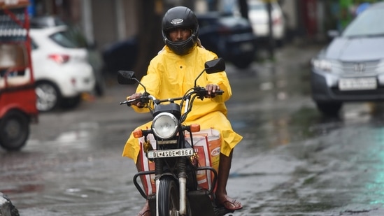 A man wearing a raincoat rides a two-wheeler during monsoon rain.(PTI)