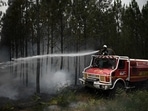 A firefighter sprays water as smoke rises from a forest fire near Louchats, as wildfires continue to spread in the Gironde region of southwestern France.