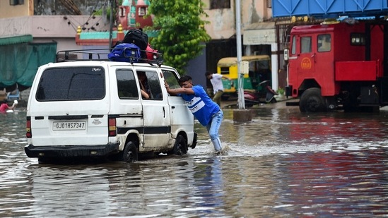 A driver of a van carrying school children, pushes the vehicle across a flooded street after heavy rains in Ahmedabad. (Photo by AFP)