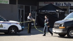 An RCMP officer moves police tape near a tent covering a body at one of three locations being investigated in regards to multiple shootings in Langley, British Columbia.