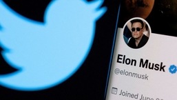 Elon Musk's twitter account is seen on a smartphone in front of the Twitter logo